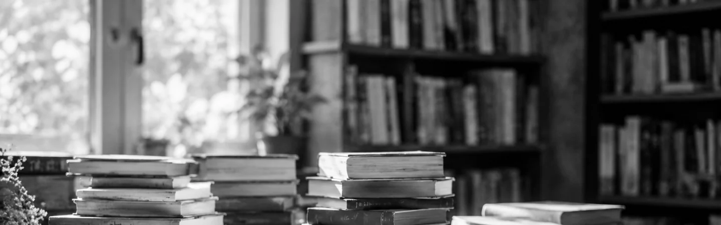 Stacks of books on a table in front of a wall of library shelves