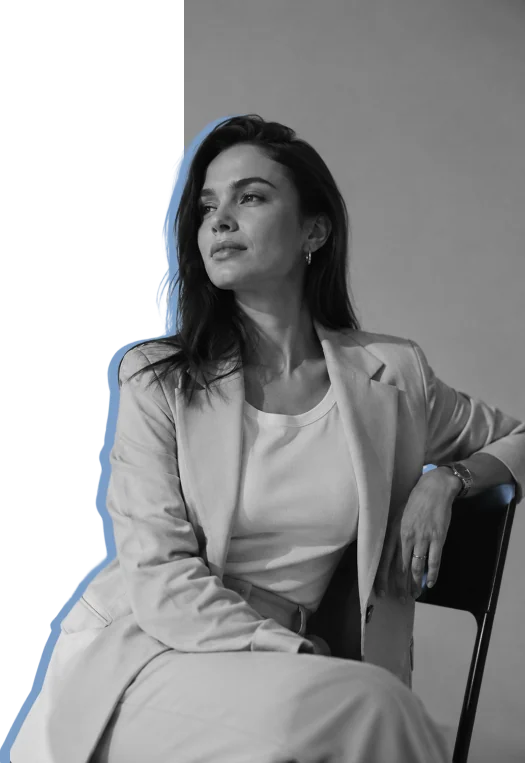 A consultant in a light suit seated against a studio wall, a Vista Blue silhouette offset behind her