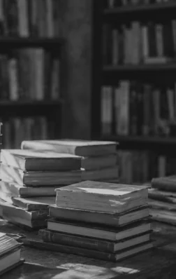 Stacks of books on a table in front of a library shelf