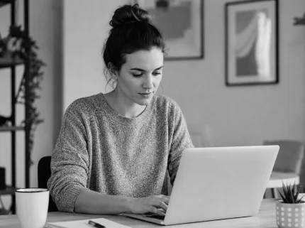 A woman writing at a laptop at a desk in a bright home office