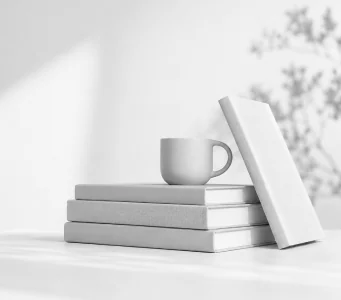 A stack of plain grey books with a mug and an upright volume leaning against them