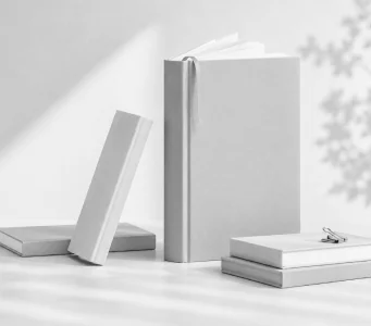 A plain grey hardback standing open-ribboned beside two flat books and a leaning cover