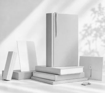 A tall grey hardback on a plinth of stacked books, with a folder and loose covers around it